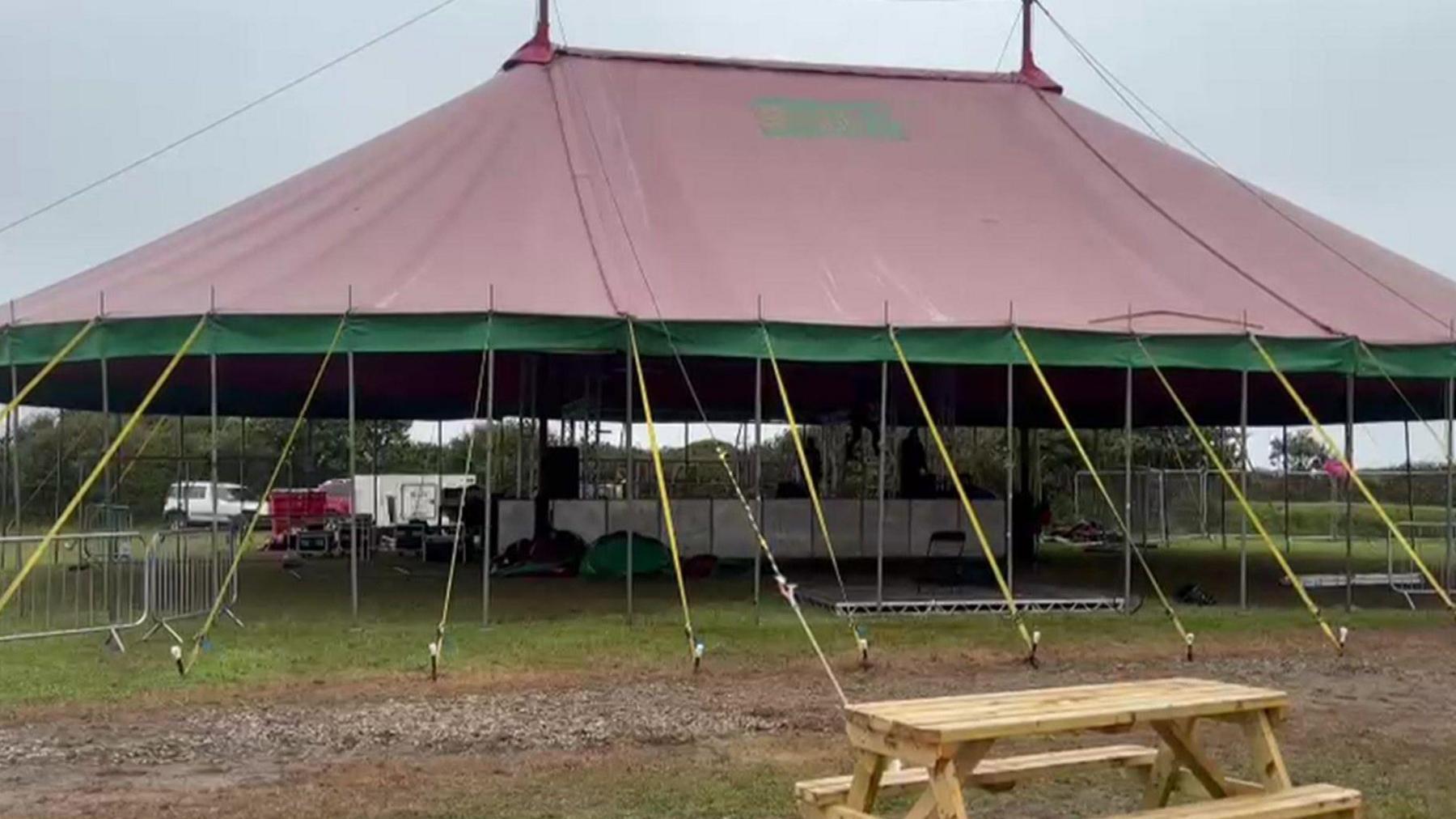 A marquee tent in a field. The ground is visibly muddy and the sky is grey with cloud.