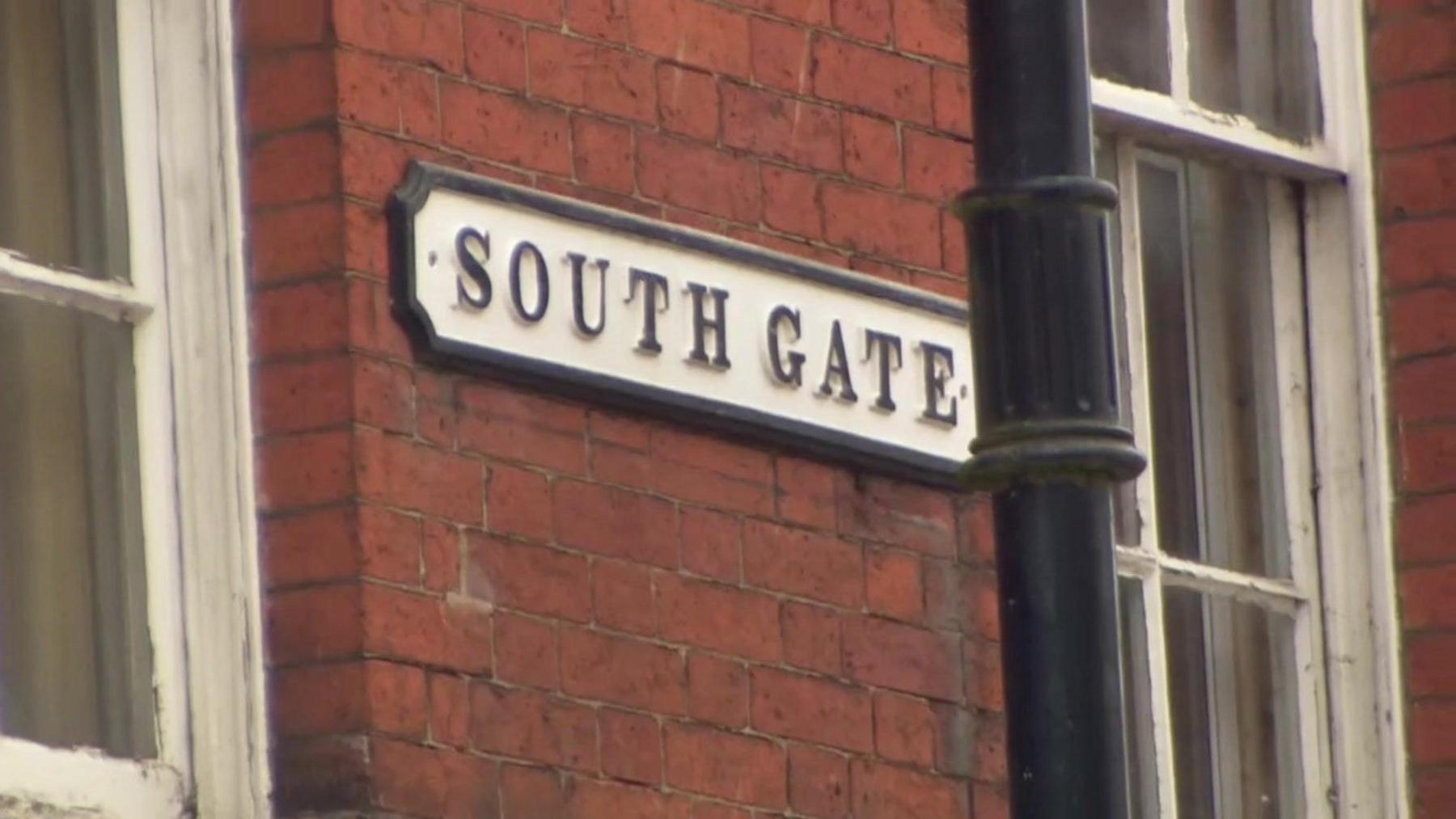 A street sign on the brick wall of a building that reads South Gate