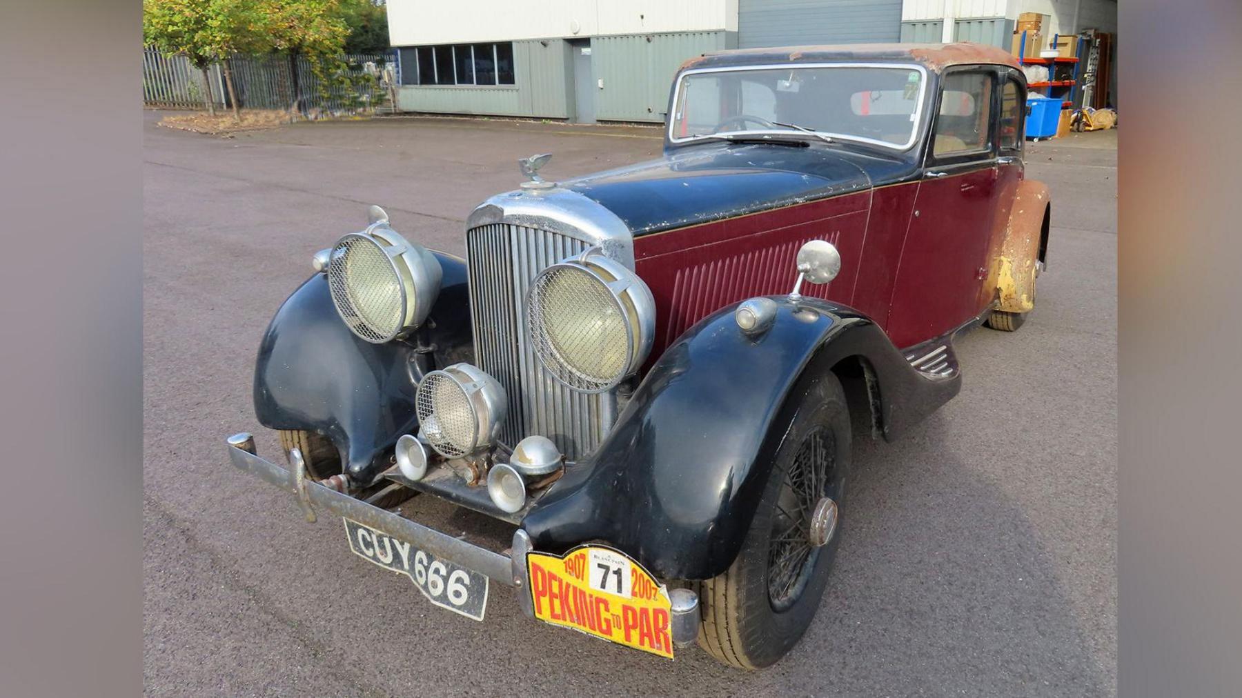 A vintage car, with large headlamps and black bumpers, and a dark red body. It has the iconic Bentley insignia on the front.