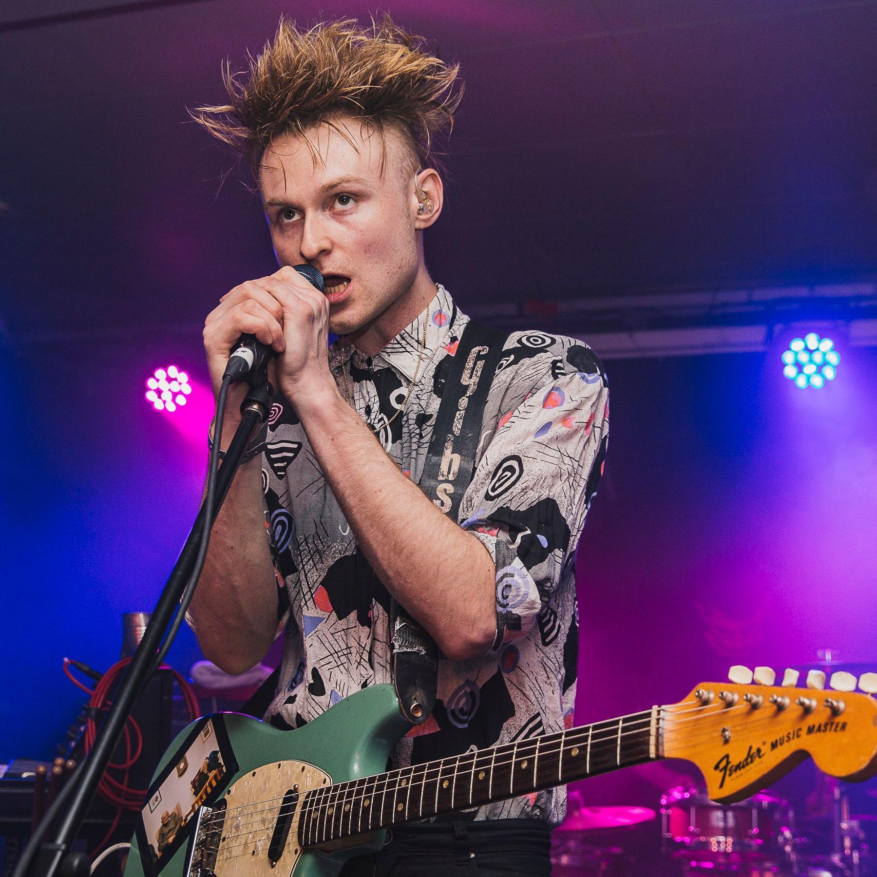 Sam Battle on stage in 2015, singing with both hands grasping a microphone and a guitar around his neck