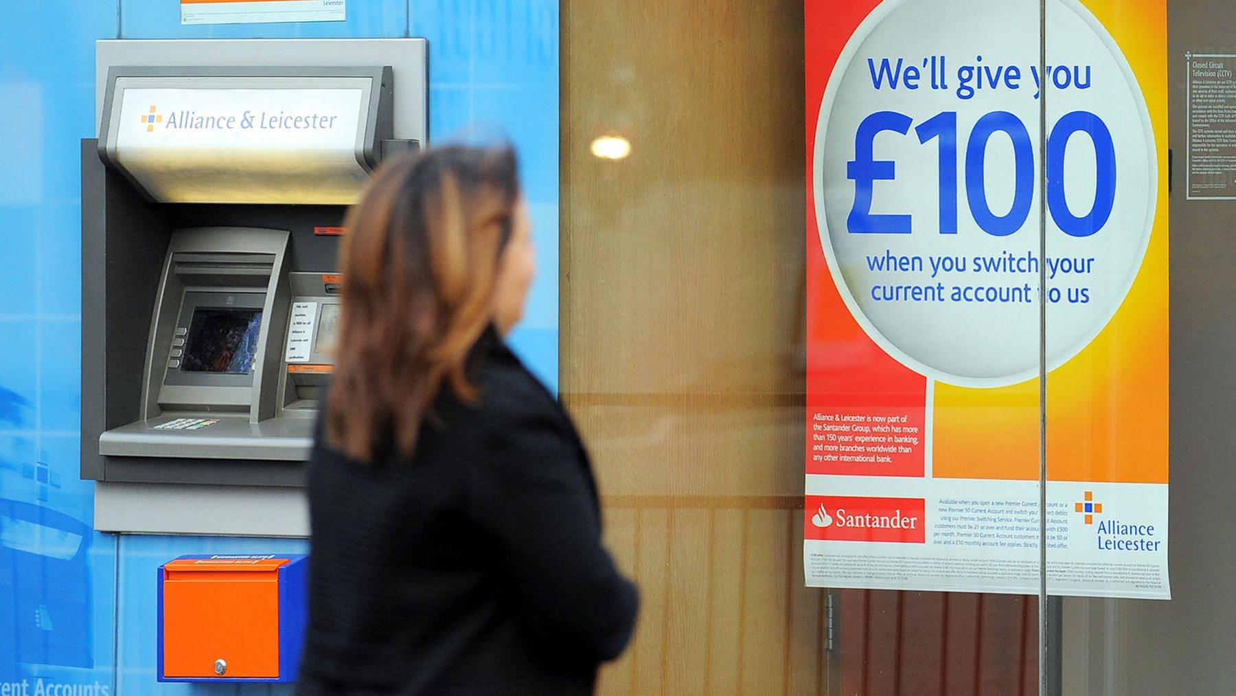 Woman wearing a dark coat looks at a sign that reads: Sort out your finances. We'll give you £100 when you switch your current account to us.