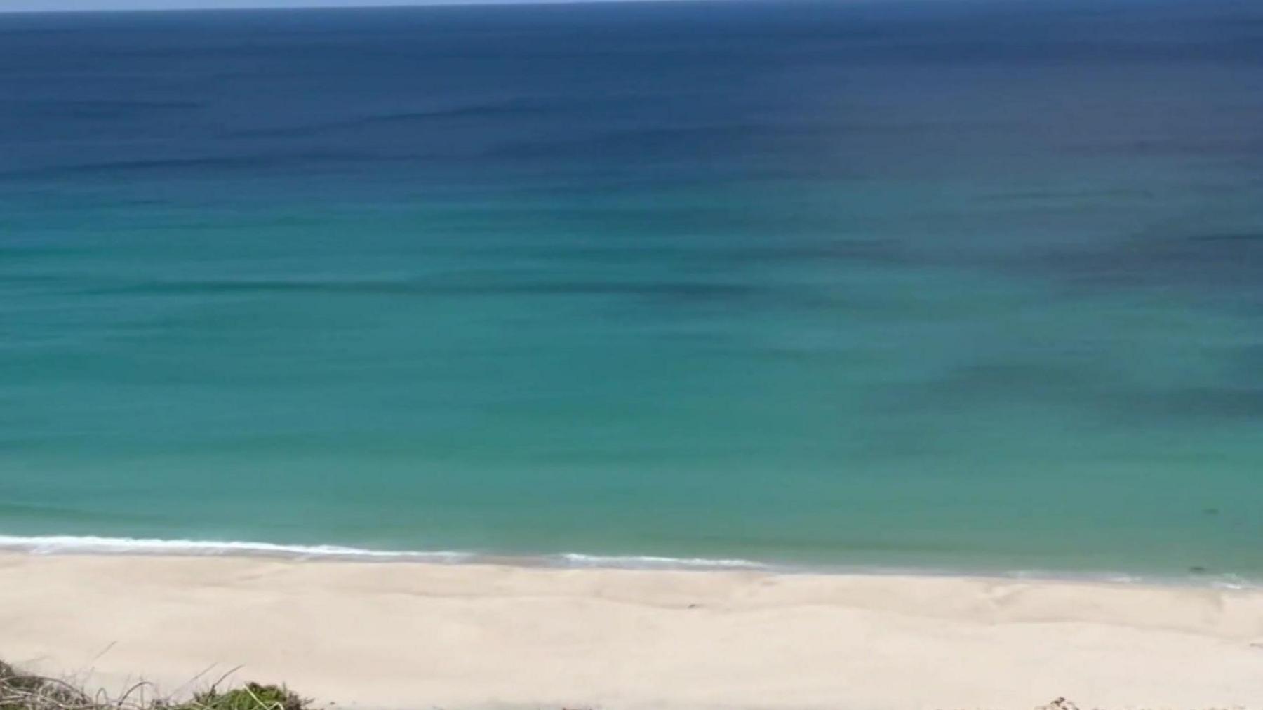 A sandy beach with blue sea beyond looked at from a cliff.