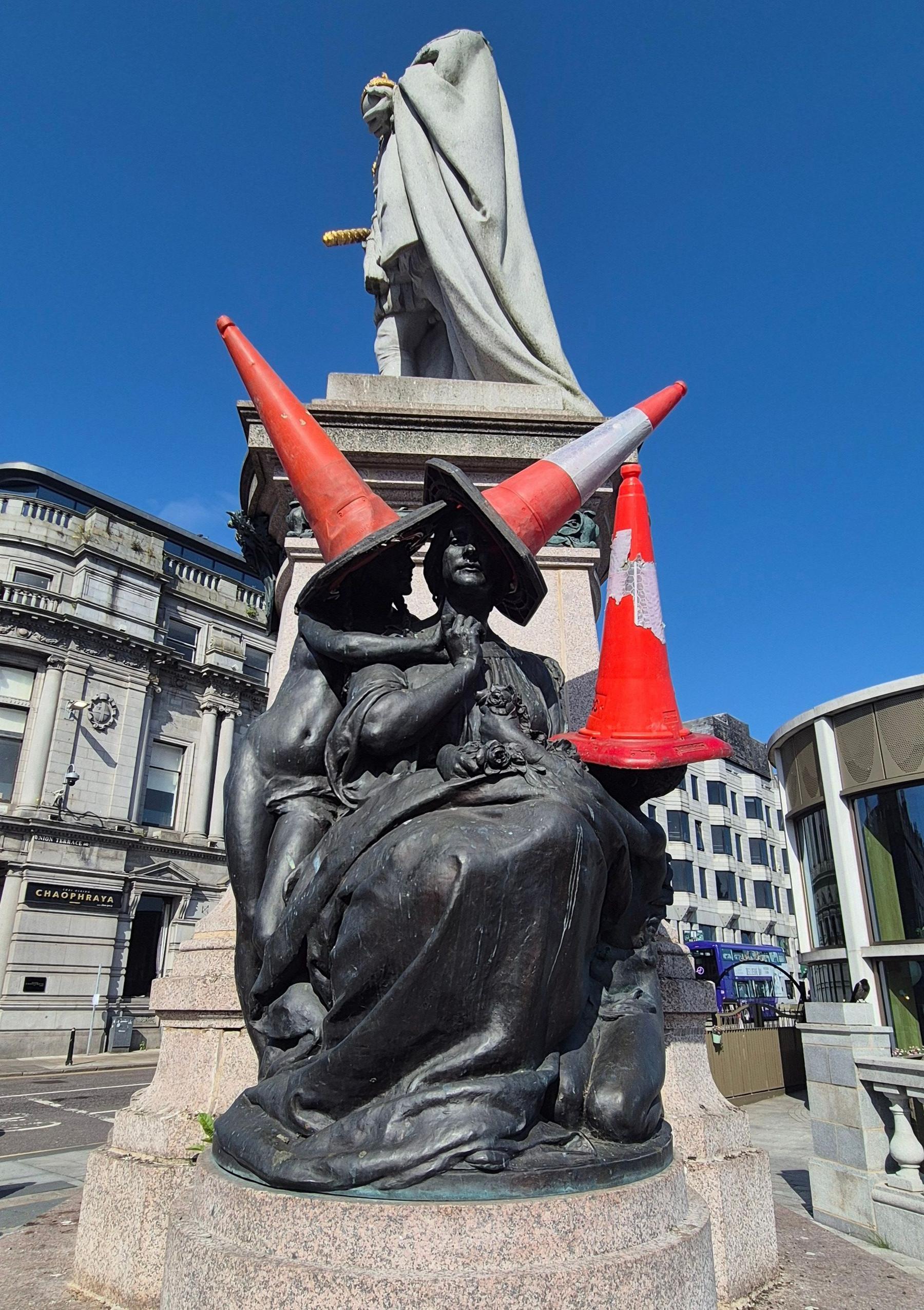 A dark metal statue with three cones on top of it