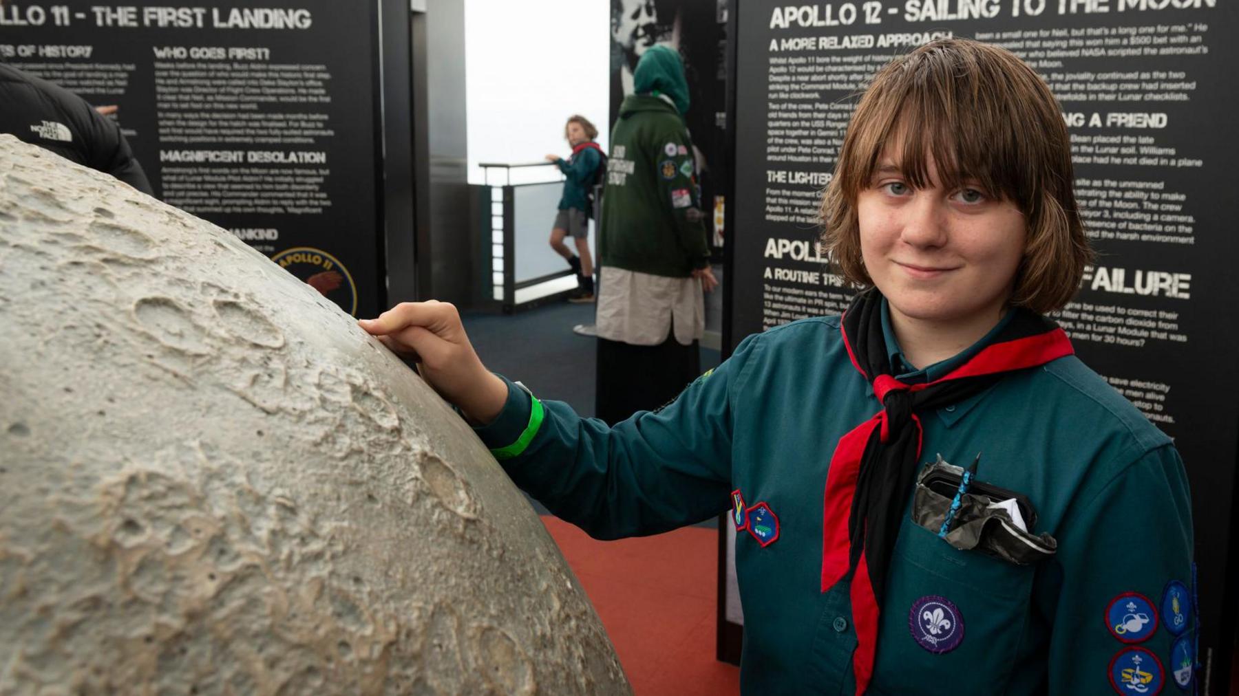 A boy scout has his hand on a large scale model of the moon