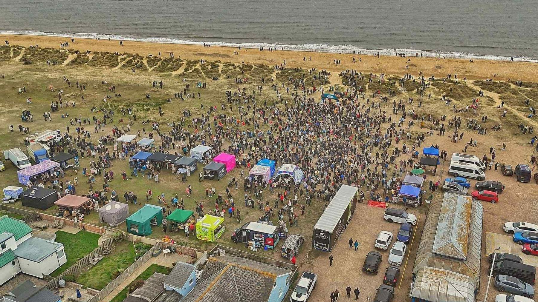 An aerial view of the beach with hundreds of people and dogs as well as tents and stands. 