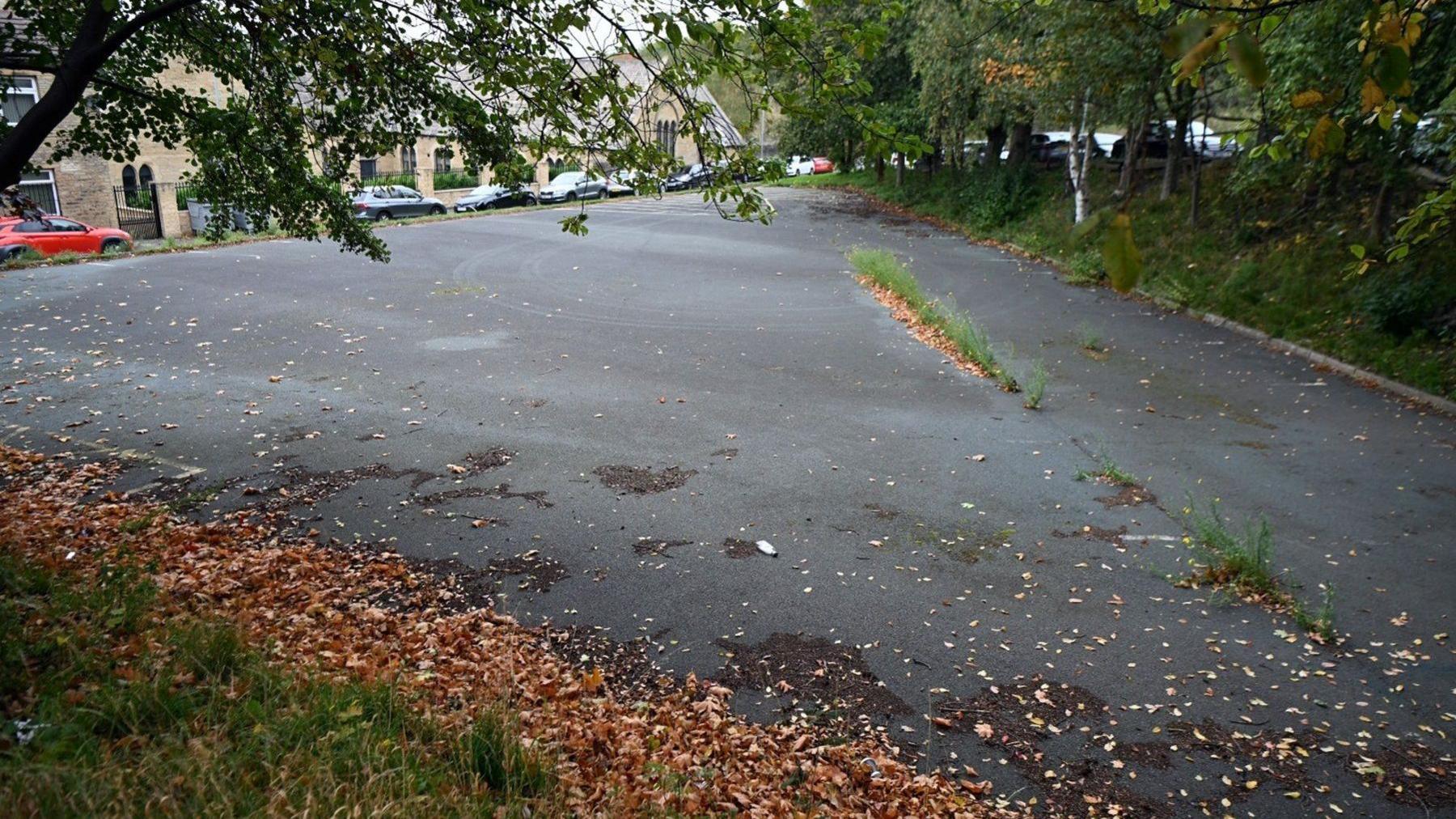 An empty car park, with autumn leaves lining the border between the concrete and surrounding grass