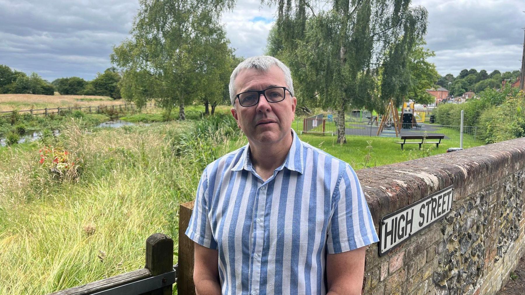 Robert Gill, in a stripy short-sleeved shirt, looking concerned as he stands close to the River Misbourne