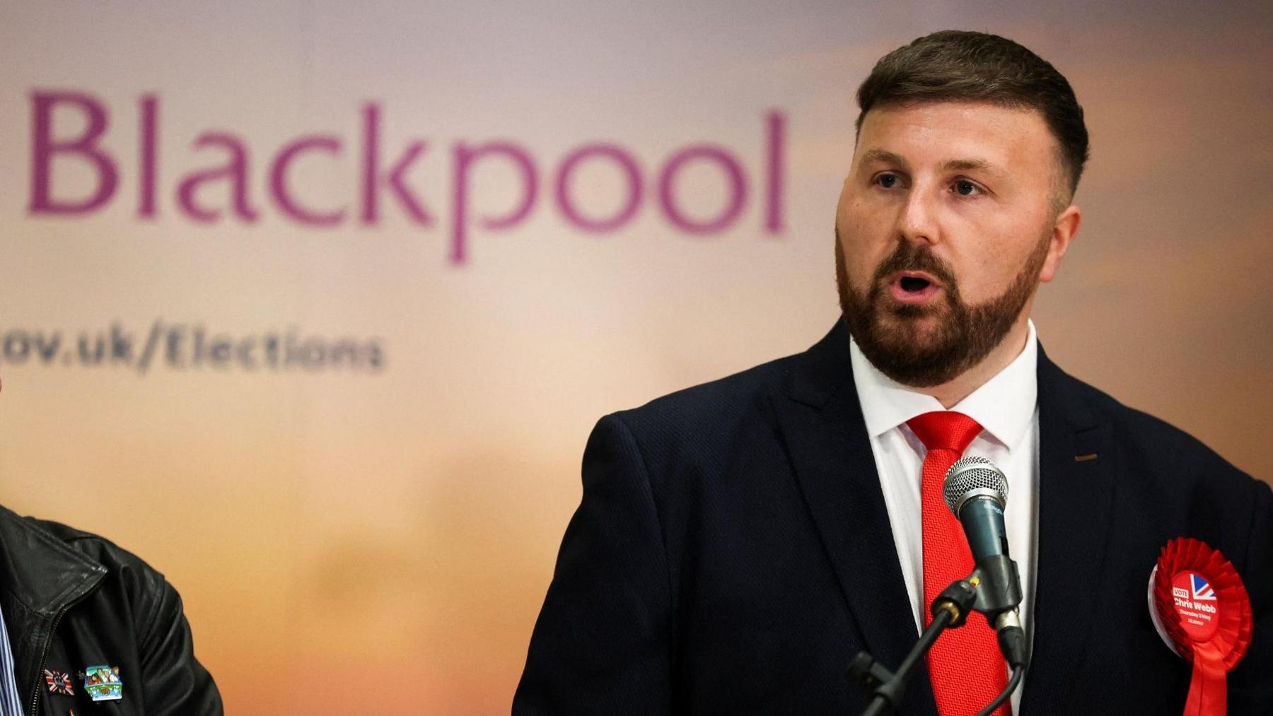 Chris Webb speaks on stage at his election in May in front of a sign saying Blackpool