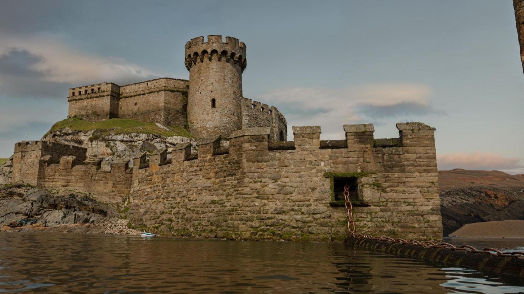 The computer generated image shows a large chain laying across the entrance of a harbour. Its sat in the water. Behind it you can see a single turret of a fort that sits over the opening to Sutton Harbour.
