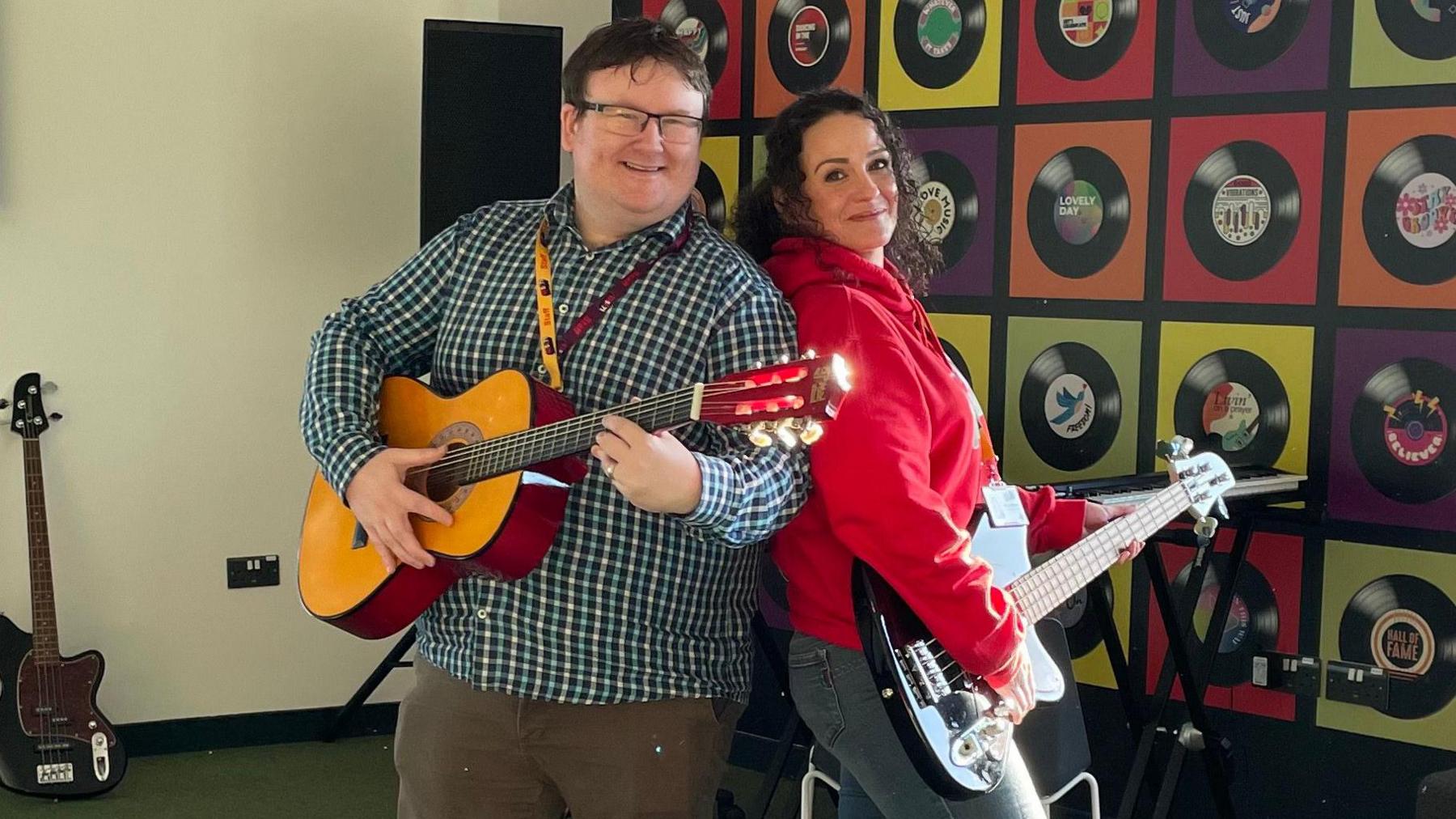 Gareth Webb and Holly Hodgson from Base71 are stood back to back in the youth hub's music hub, holding guitars.