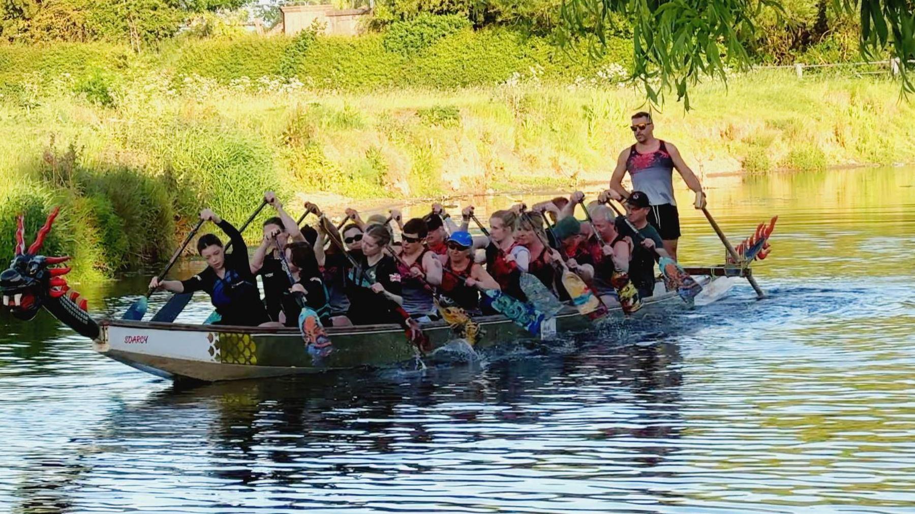 A team of dragon boat racers rowing a boat on a river.