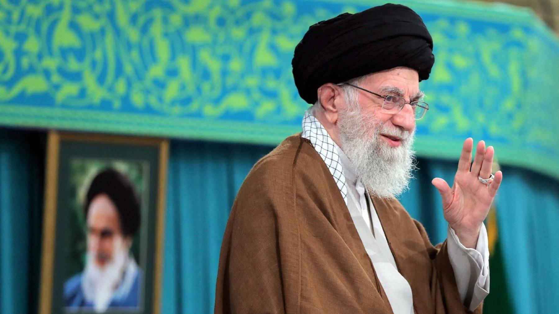 Iranian Supreme Leader Ali Khamenei wearing a black turban with a portrait behind him