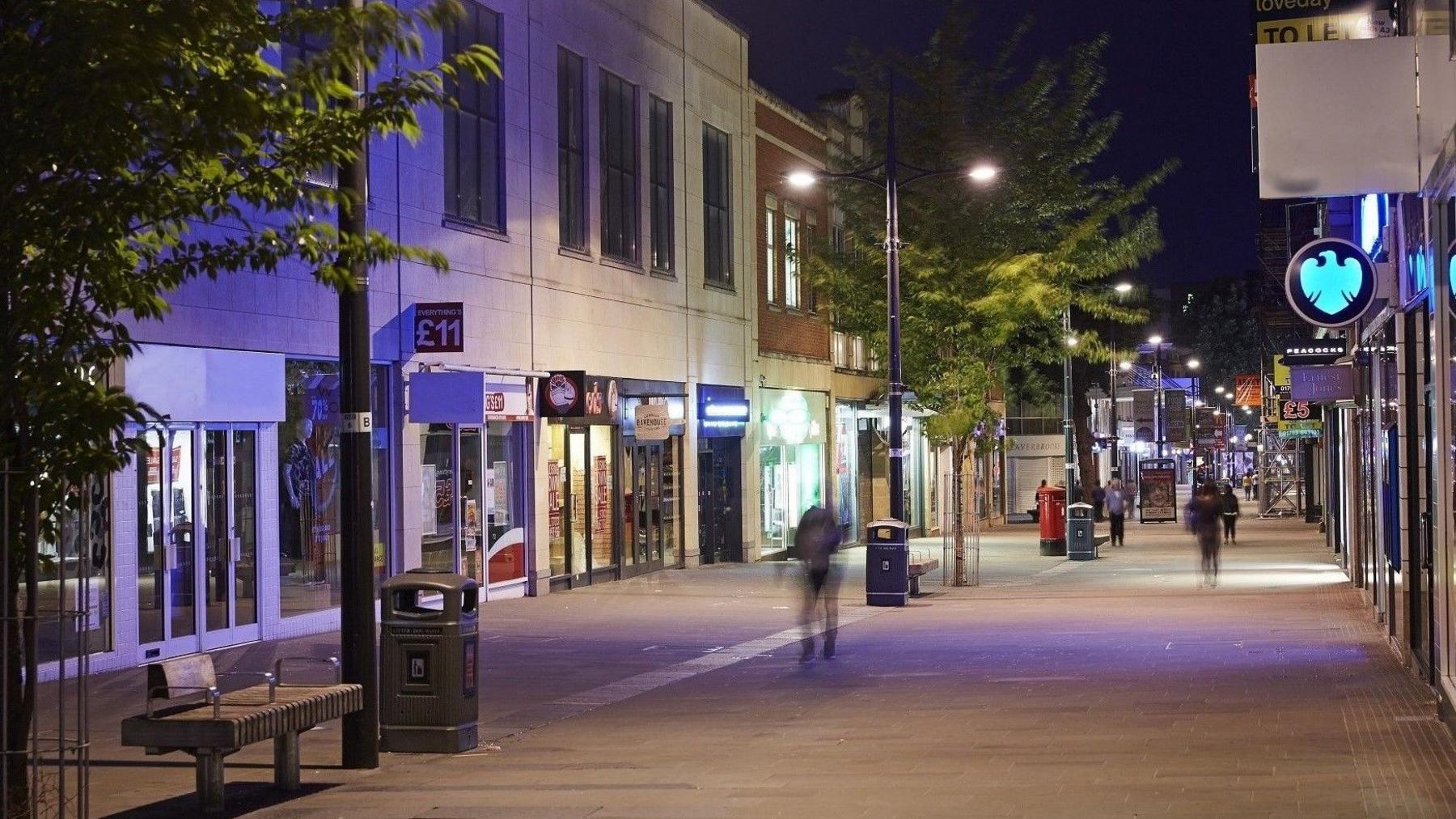 A night time shot of the centre of Swindon with people walking between rows of shops