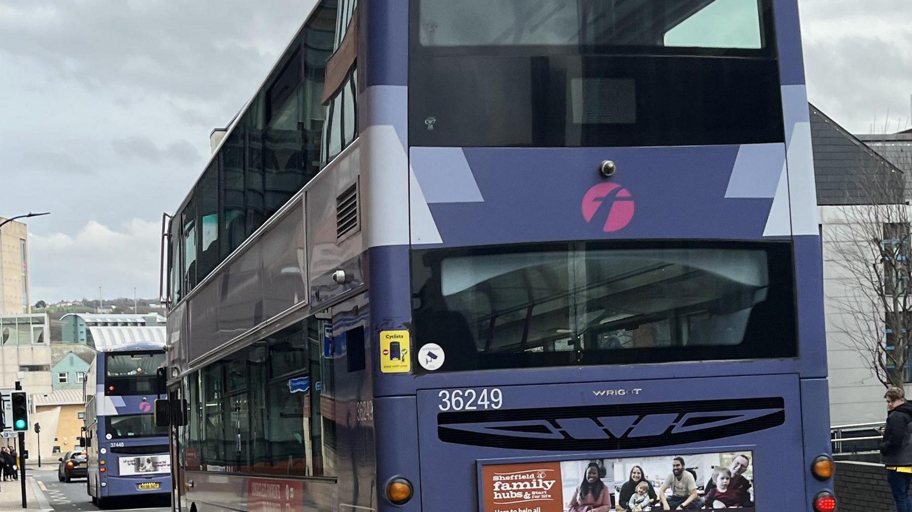 A First-branded bus driving down a city street, with another further up the road.