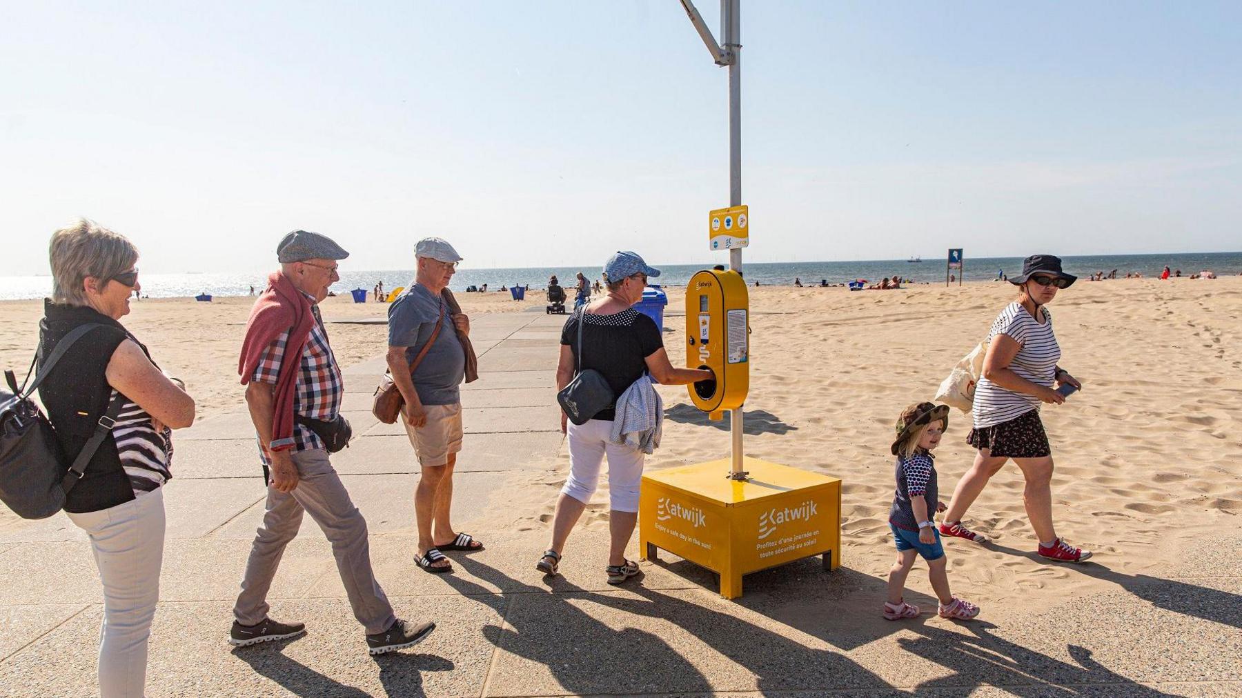 People line up to apply suntan lotion provided for free by the local government on a beach at Katwijk aan Zee, Netherlands