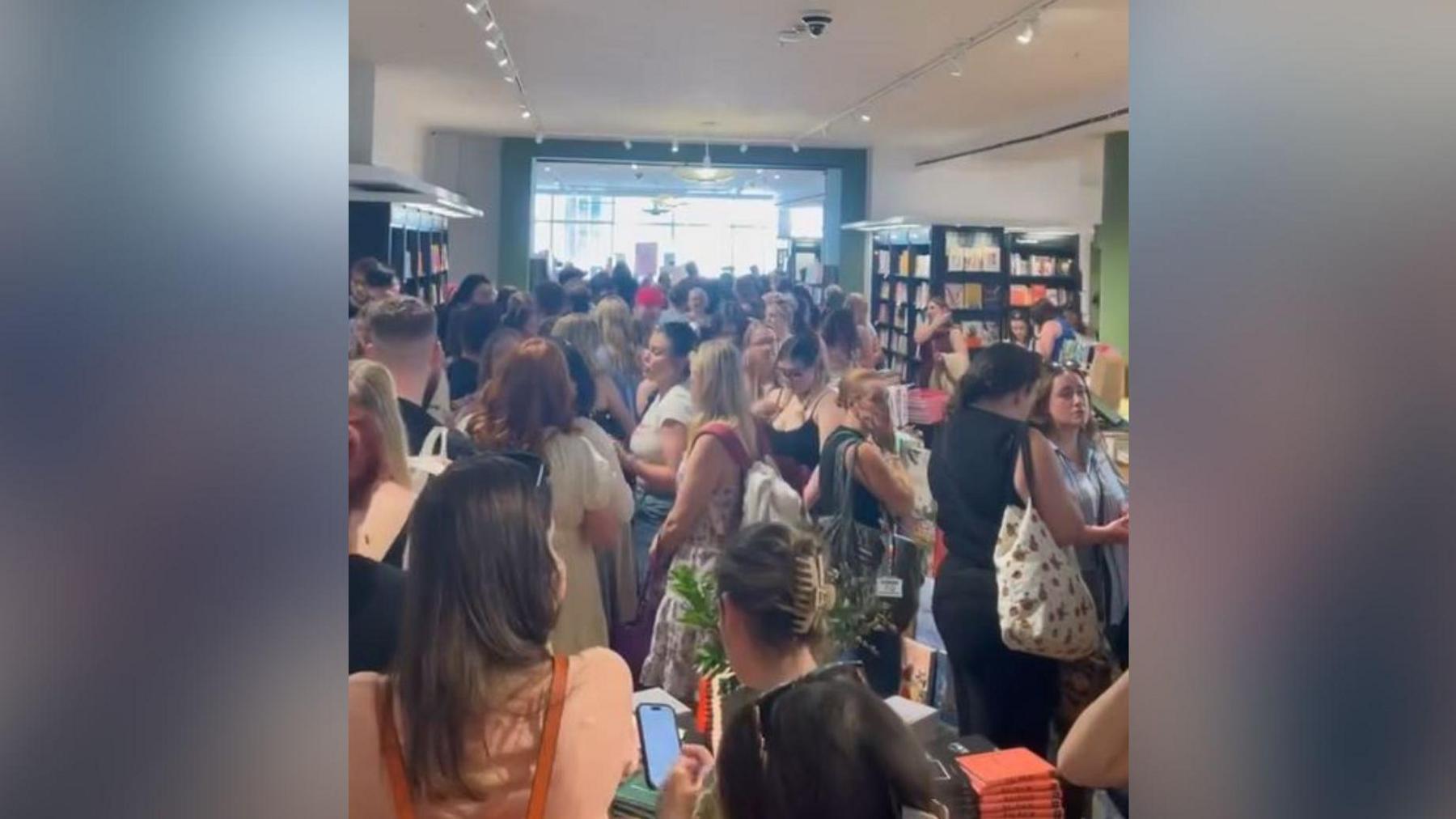 A picture inside a large, busy bookshop, with groups of people stretching back towards the far, windowed wall.