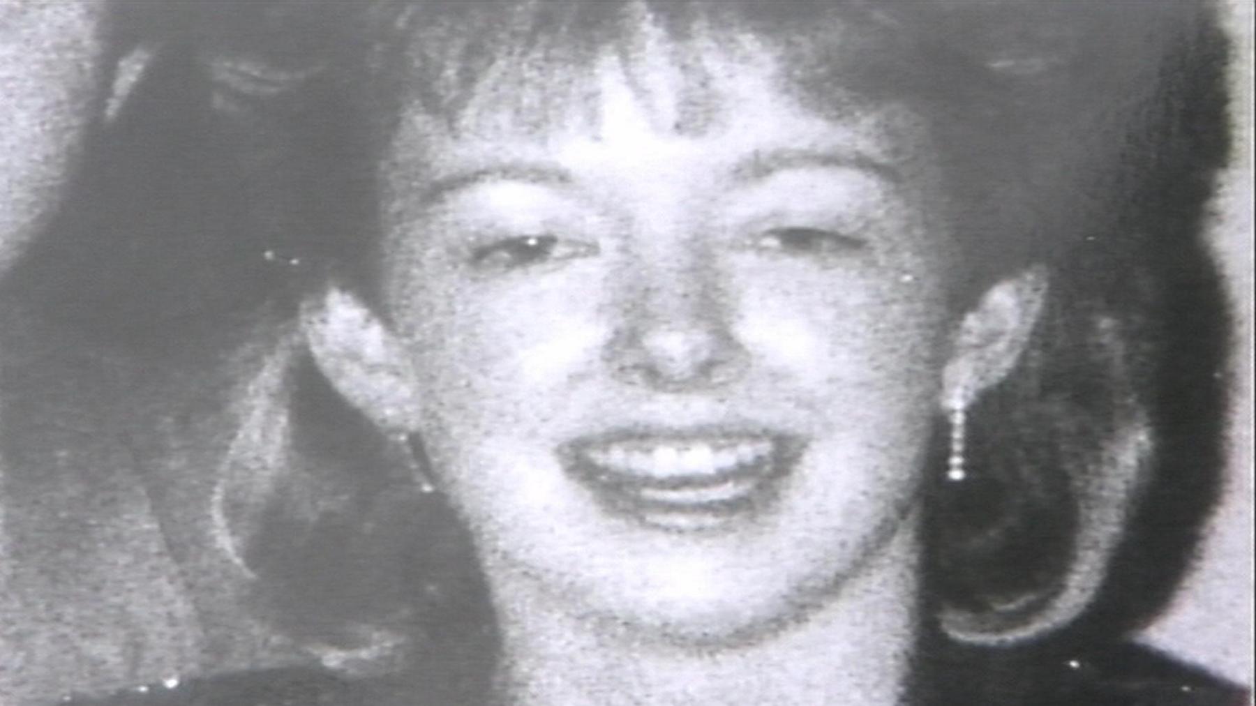 A black-and-white photograph of Diane Sindall, who has her hair cut into a fringe. She is smiling at the camera.