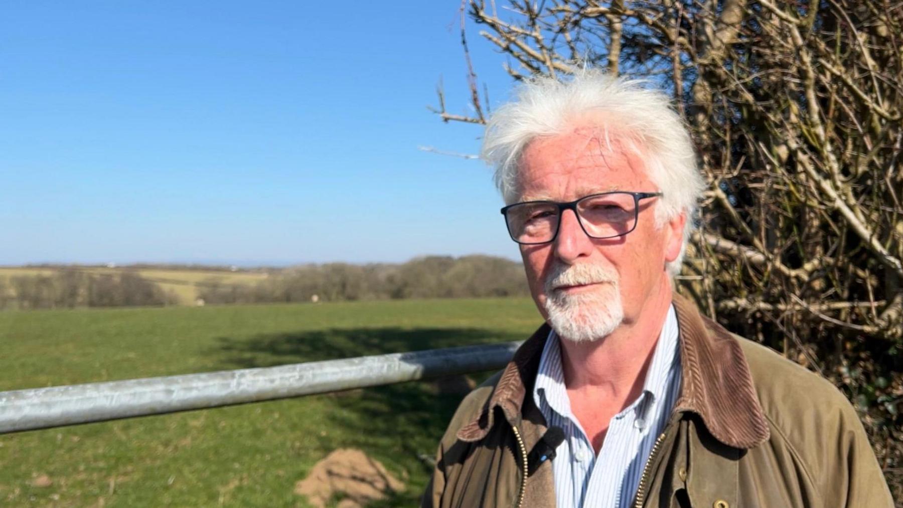 Steve Crowther from the Campaign for the Protection of Rural England in a striped shirt and a green jacket standing overlooking the solar park site