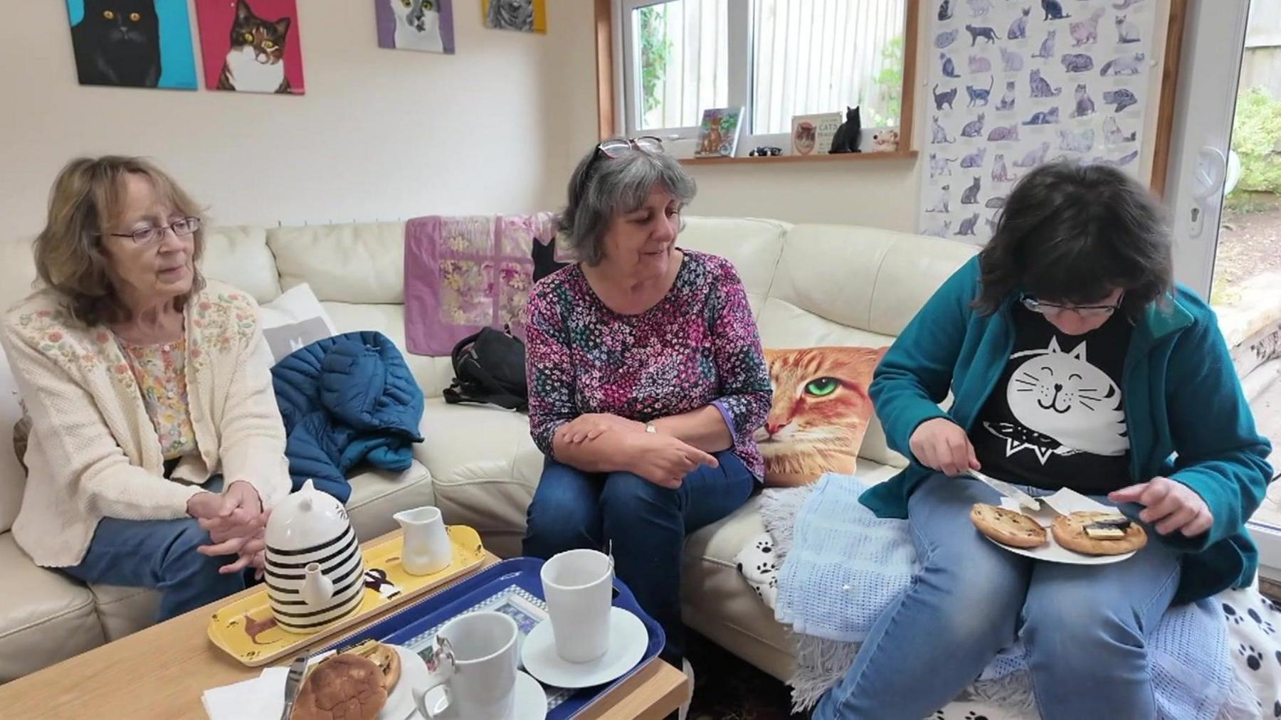 Three female customers sitting on the sofa in the café eating cake