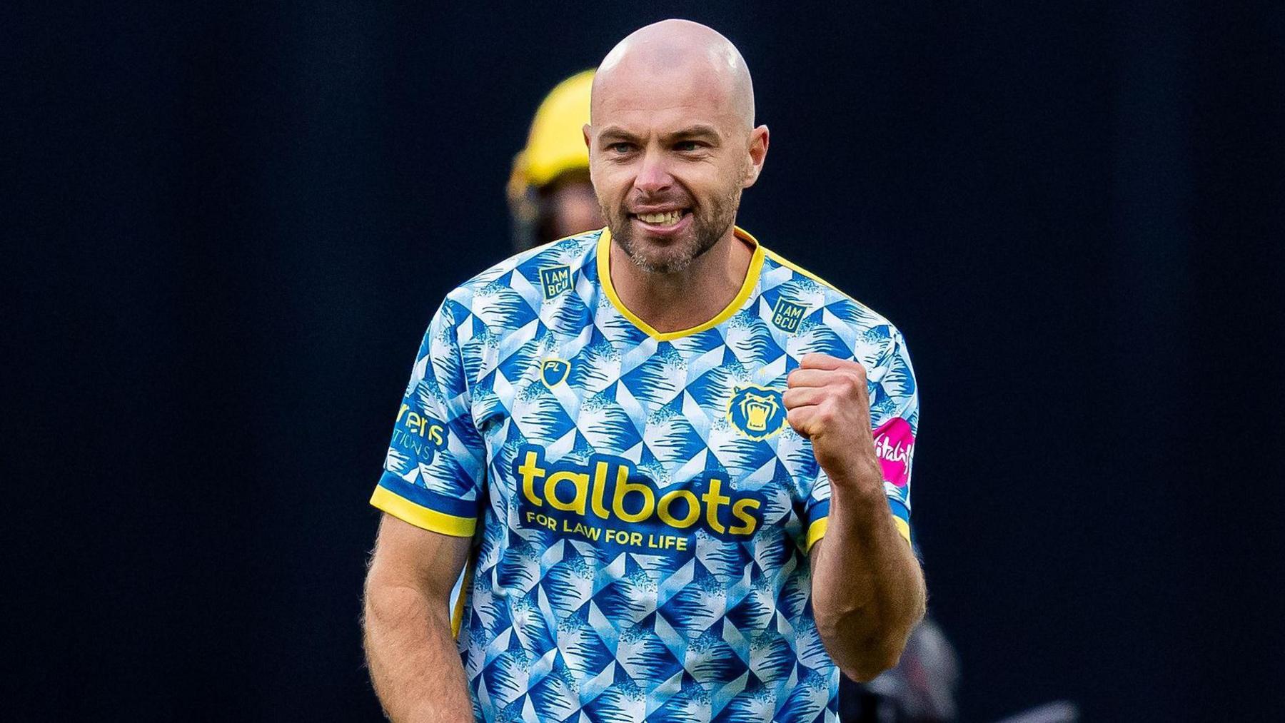 Jake Lintott raises his fist in celebration, wearing Birmingham Bears' blue, white and yellow patterned jersey
