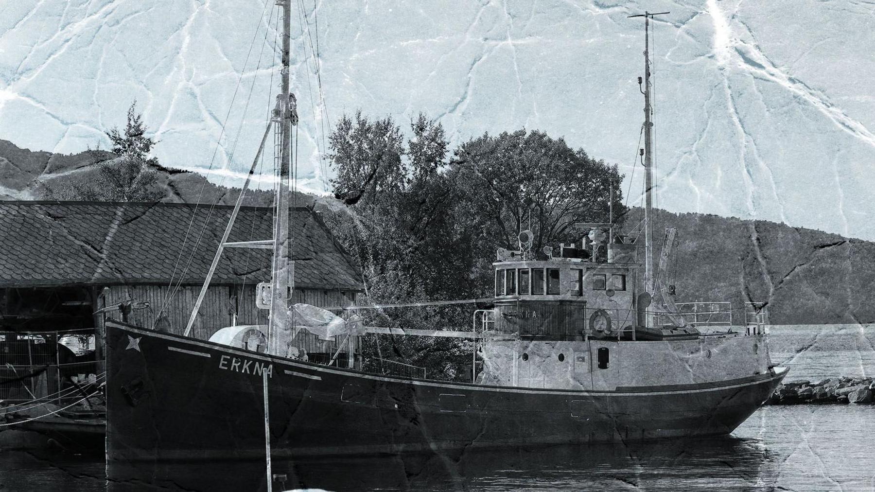 A black and white picture of the the M/K Erkna - a medium sized boat stationed by the shore with a building nearby. The picture appears to have been scanned so you can see lots of lines where it was folded.