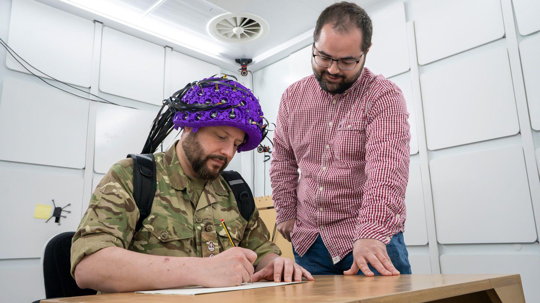 Lt Col James Mitchell undertaking writing task whilst being scanned, being monitored by PhD student Daniel Ford.