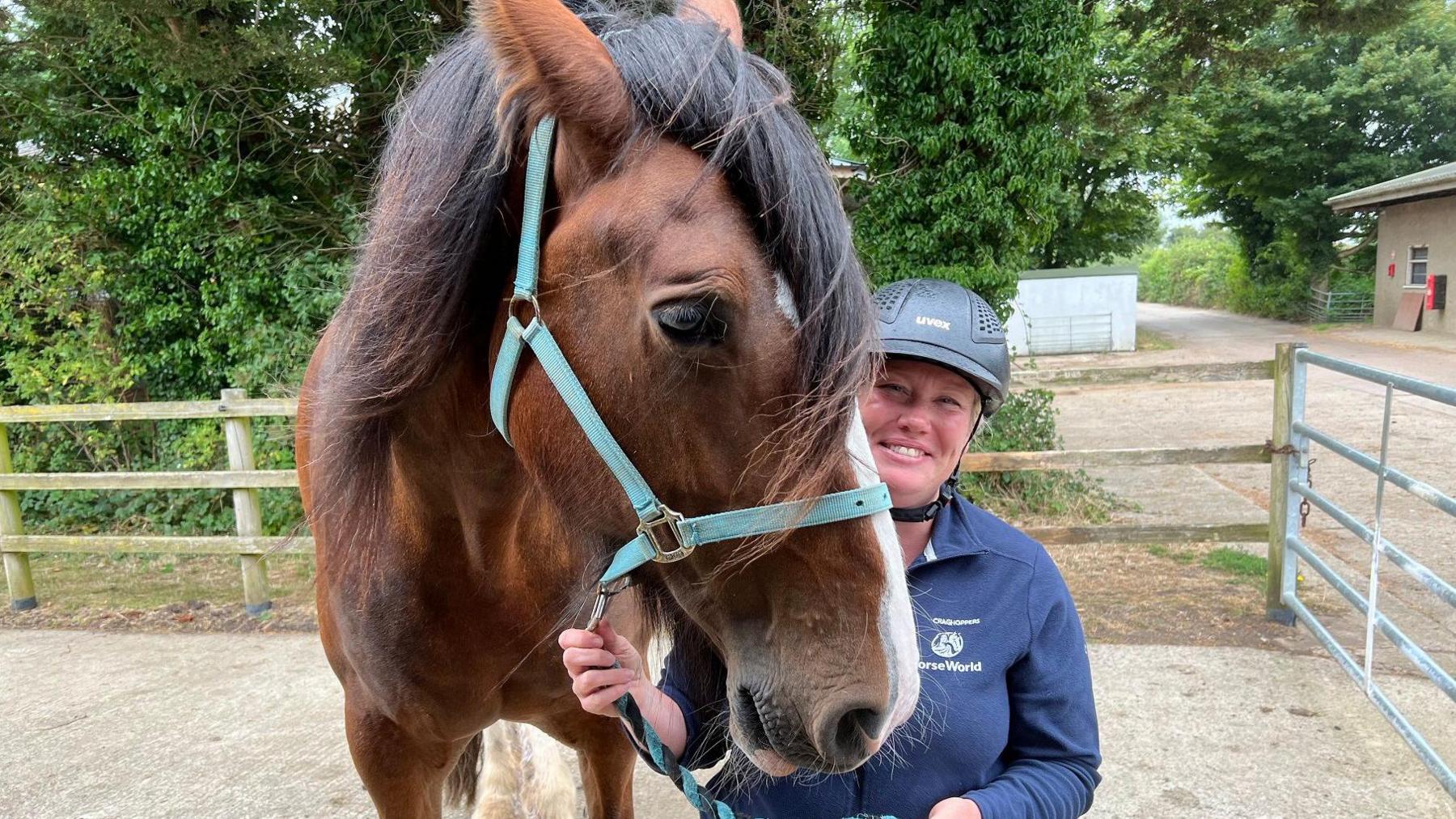 A woman holds a horse by the reins at Horseworld in Whitchurch near Bristol. She is smiling and wearing a blue top and blue helmet