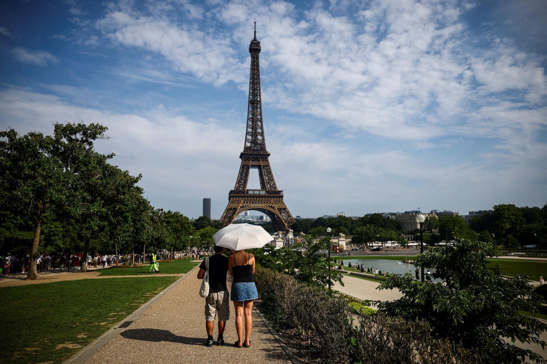 Peoole walking under and umbrella in the heat towards the Eiffel Tower.