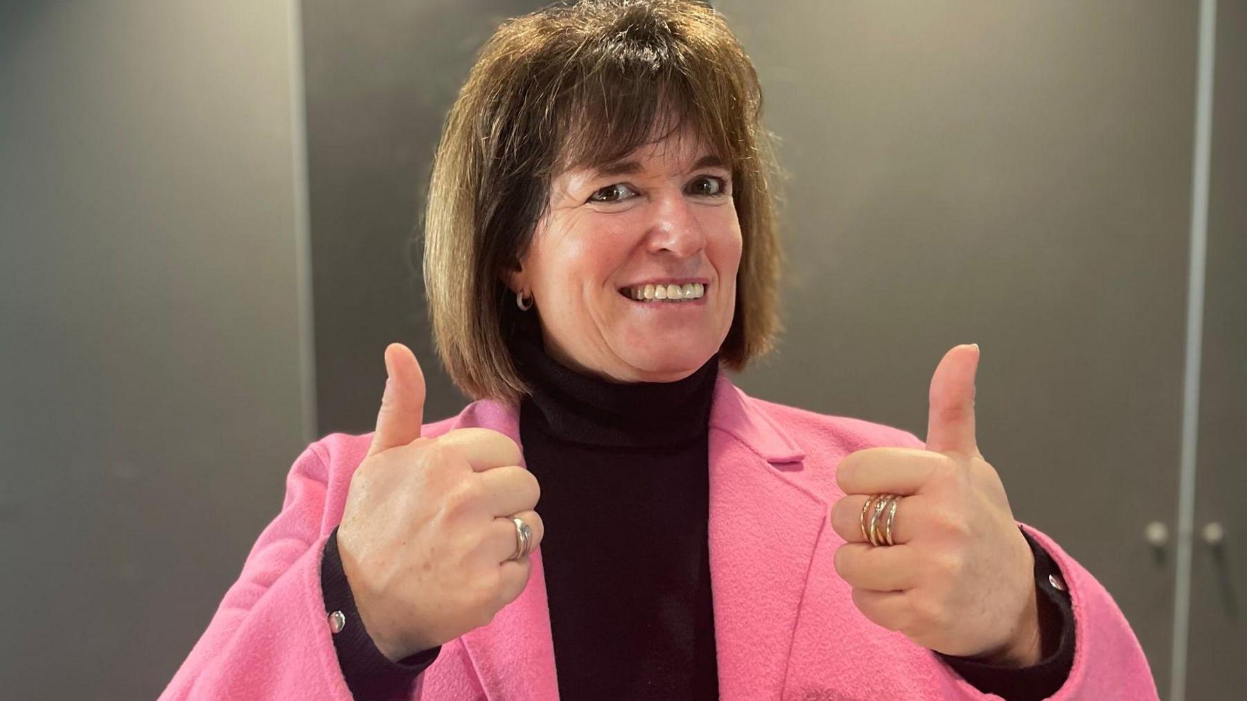 A woman is giving a British Sign Language double thumbs up sign