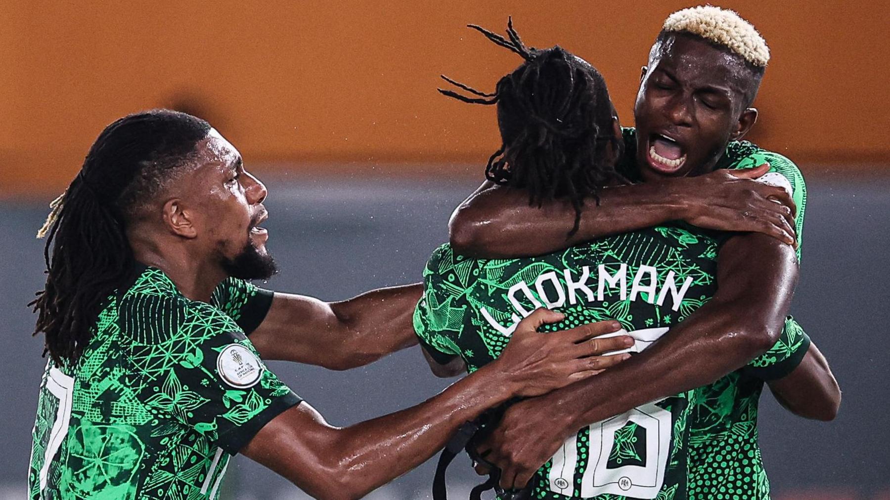 Nigeria players celebrate a goal, with Victor Osimhen giving Ademola Lookman, who is facing away from camera, a hug as Alex Iwobi joins the embrace from the left of the shot