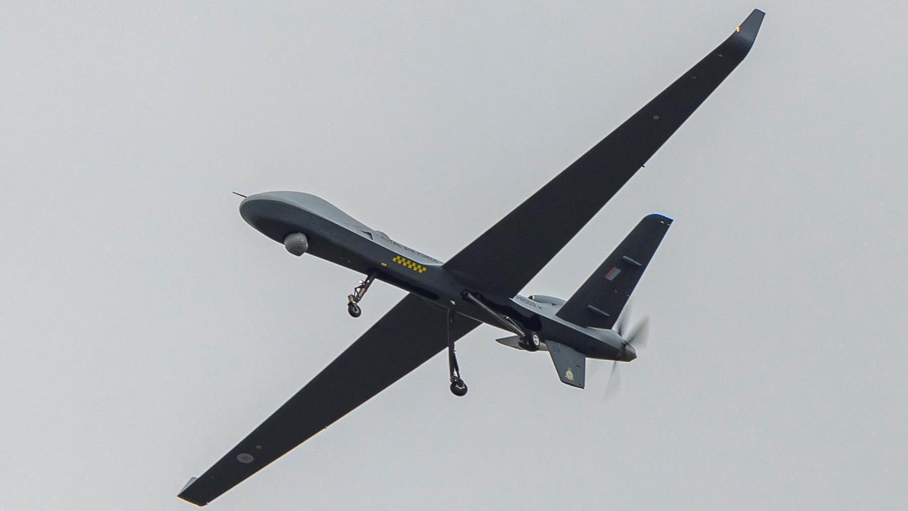 A grey and black Protector drone flying through the sky against a grey background.