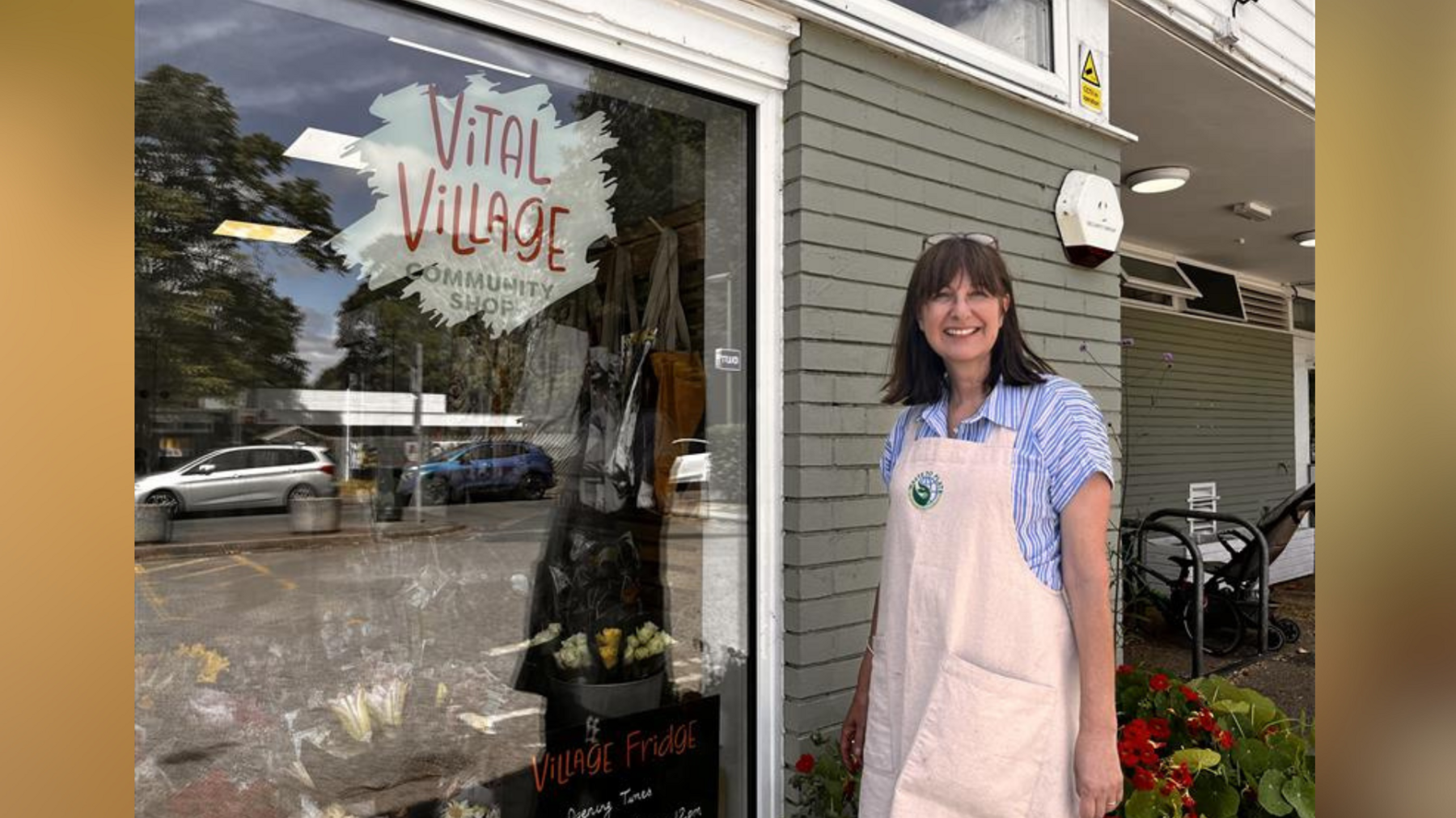 Volunteer Alison Barnett pictured outside the Vital Village community shop in Thames Ditton. Alison is wearing a short-sleeved blue striped shirt and an apron.