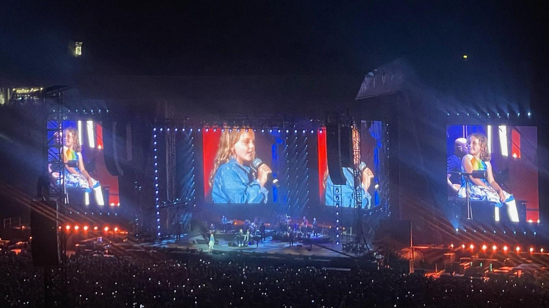 Billy Joel on stage with his daughters as the crowd looks on with their phones lit up