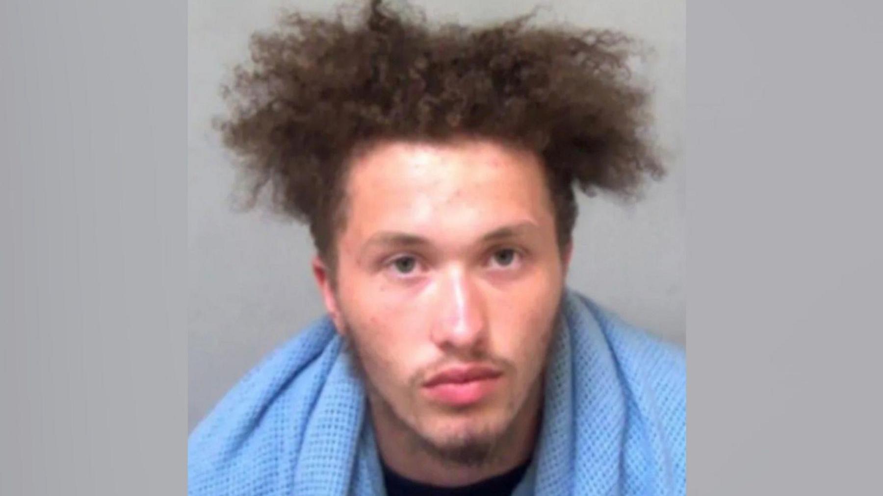 A police custody picture of a man with a blue towel or blanket around his neck.