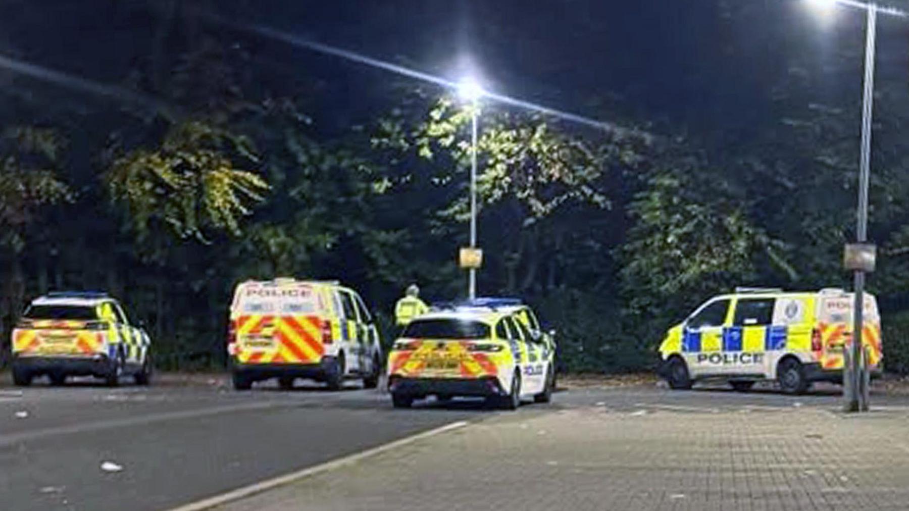 Five police vehicles in a car park in front of some trees