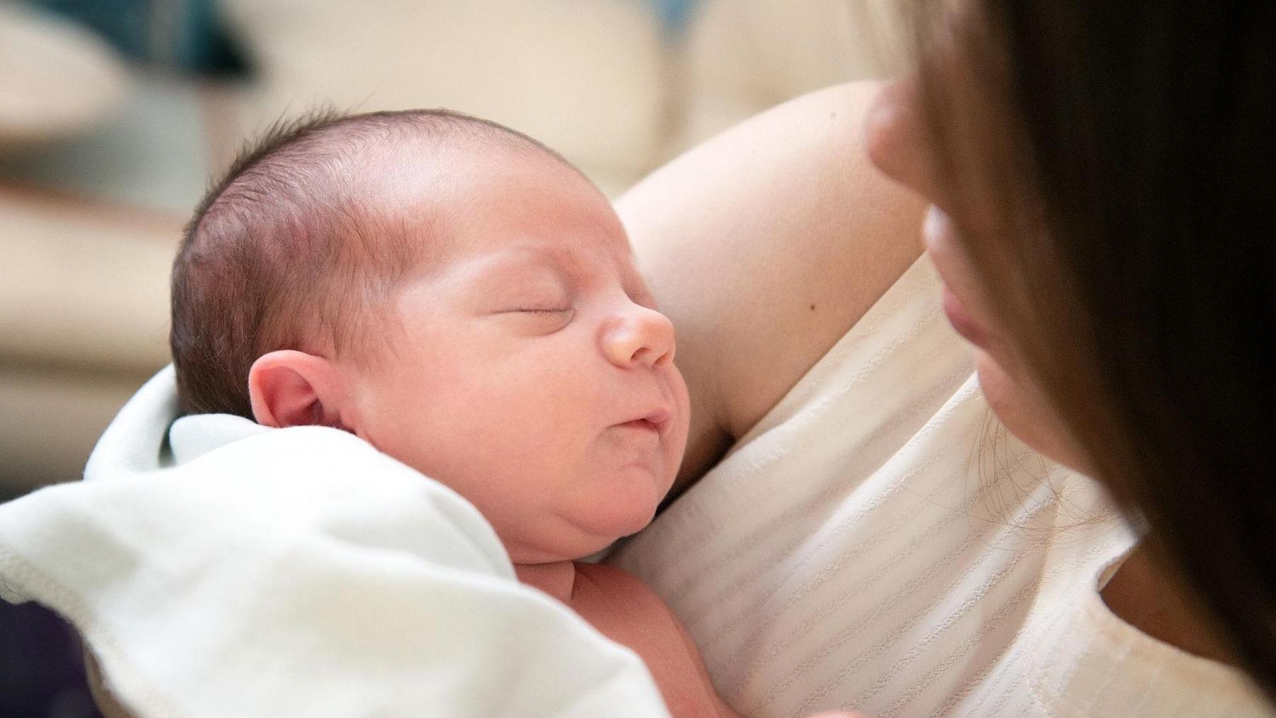 A picture of a sleeping new born baby being held by a woman.