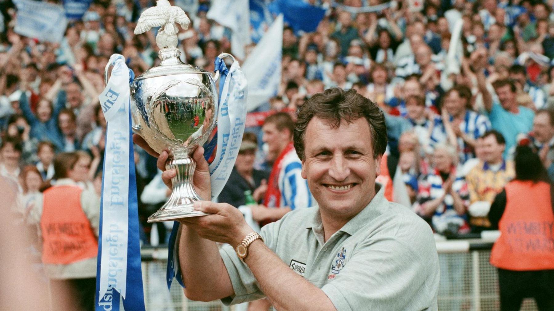 Neil Warnock holds up the play-off trophy at Wembley adorned with blue and white ribbons