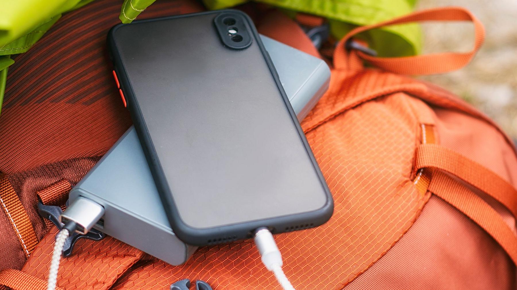 A power bank and mobile phone sit on top of an orange suitcase. They have have charging cables connected