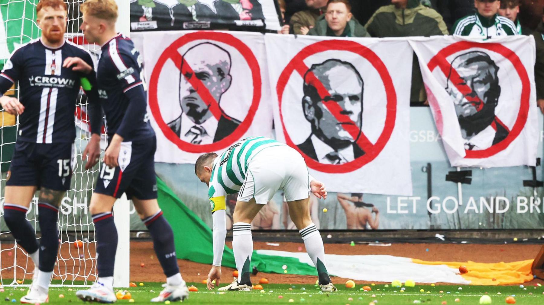 Celtic captain Callum McGregor picks up bouncy balls thrown onto the Dens Park pitch by Celtic supporters
