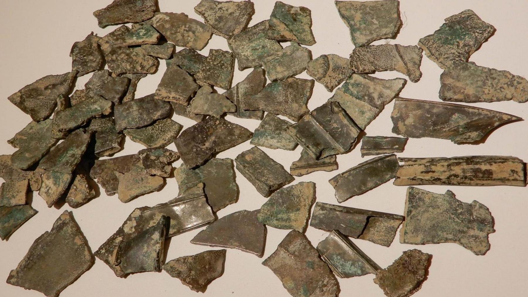 Metal fragments are spread out on a surface. They are fairly small and have jagged edges and are brown, with green tinges