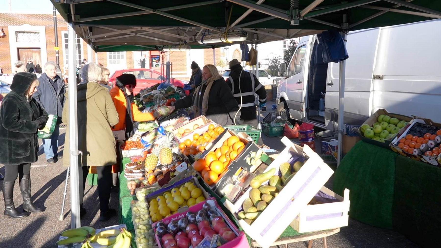 A fruit and veg stall with people looking at the fruit