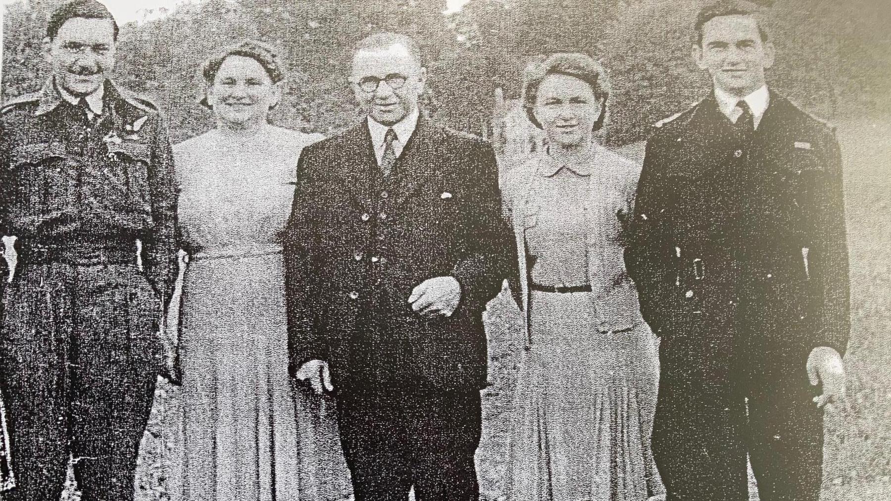 A black and white photo of Tony Bird standing with two men and two women. All the men were dark suits while the women wear dresses.