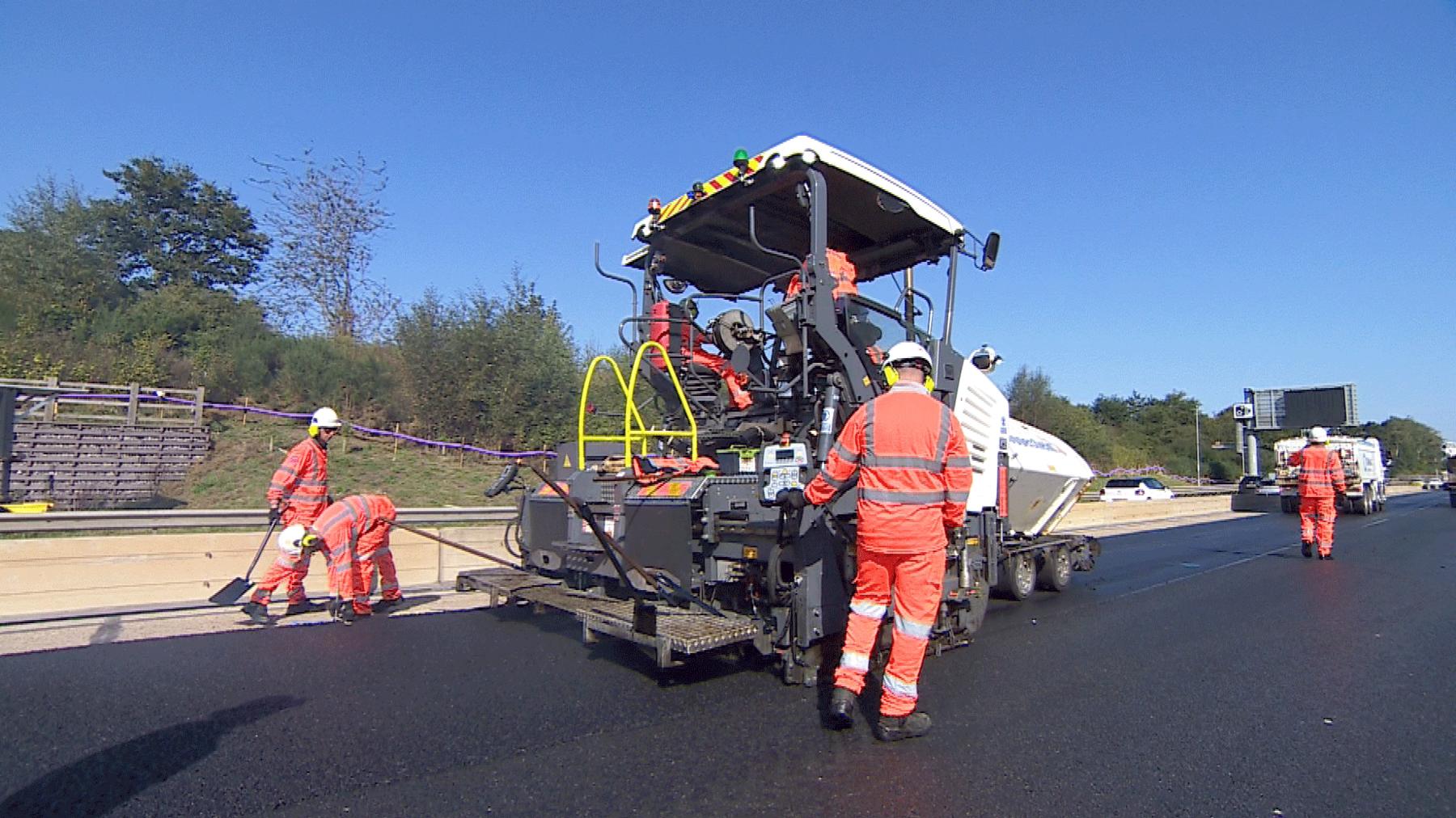 Workers attend to a contraption that lays tarmac onto the motorway near to the central reservation.