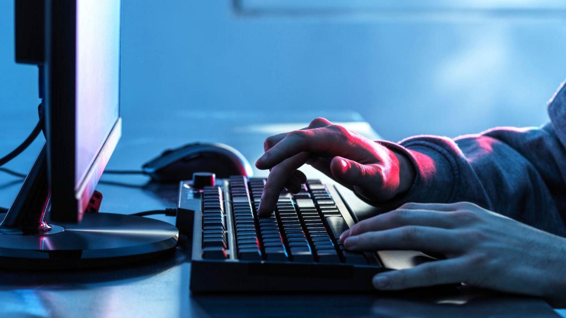 A computer viewed side on with hands on a keyboard and one finger pressing a button