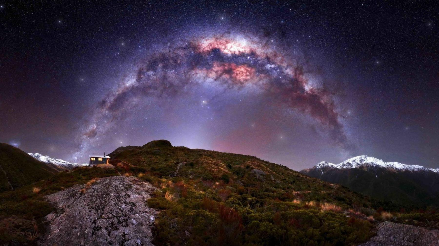 A hut in the far distance on a marshy island, with the Milky Way stretching over the sky