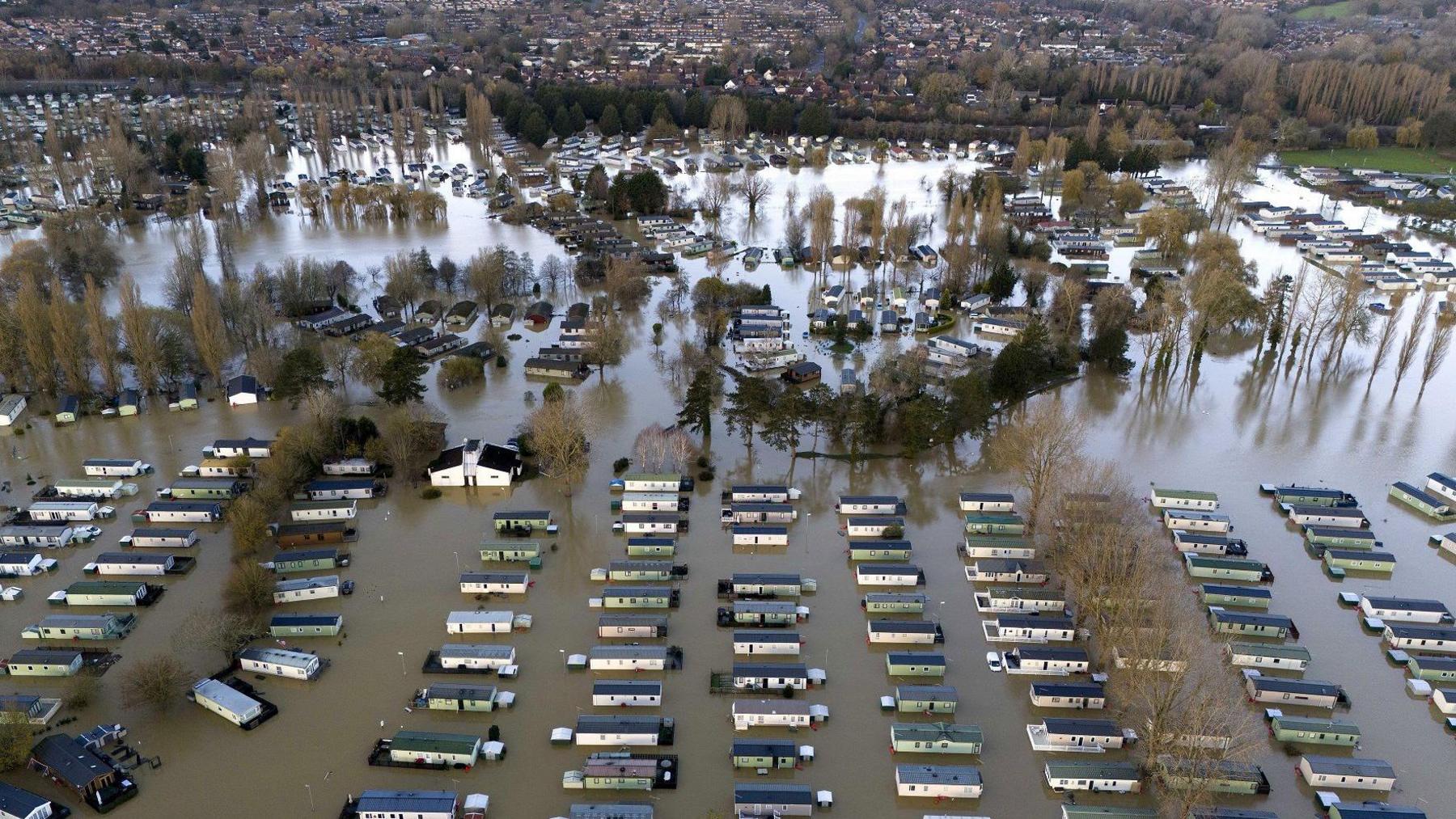 An aerial photo of the flooded Billing Aquadrome Holiday Park. There are more than 100 static caravans with flood water up to their windows and the whole site is deep in brown flood water. Houses in Northampton can be seen in the distance. 