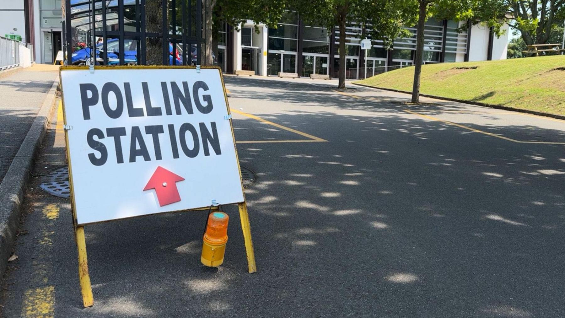 Polling station sign by car parking spaces in front of a meeting