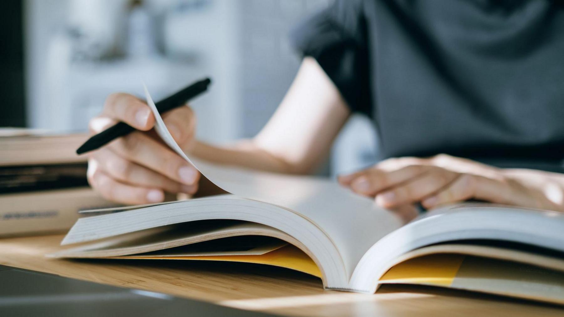 Stock image of person in grey tshirt holding a pen and flicking through a notebook