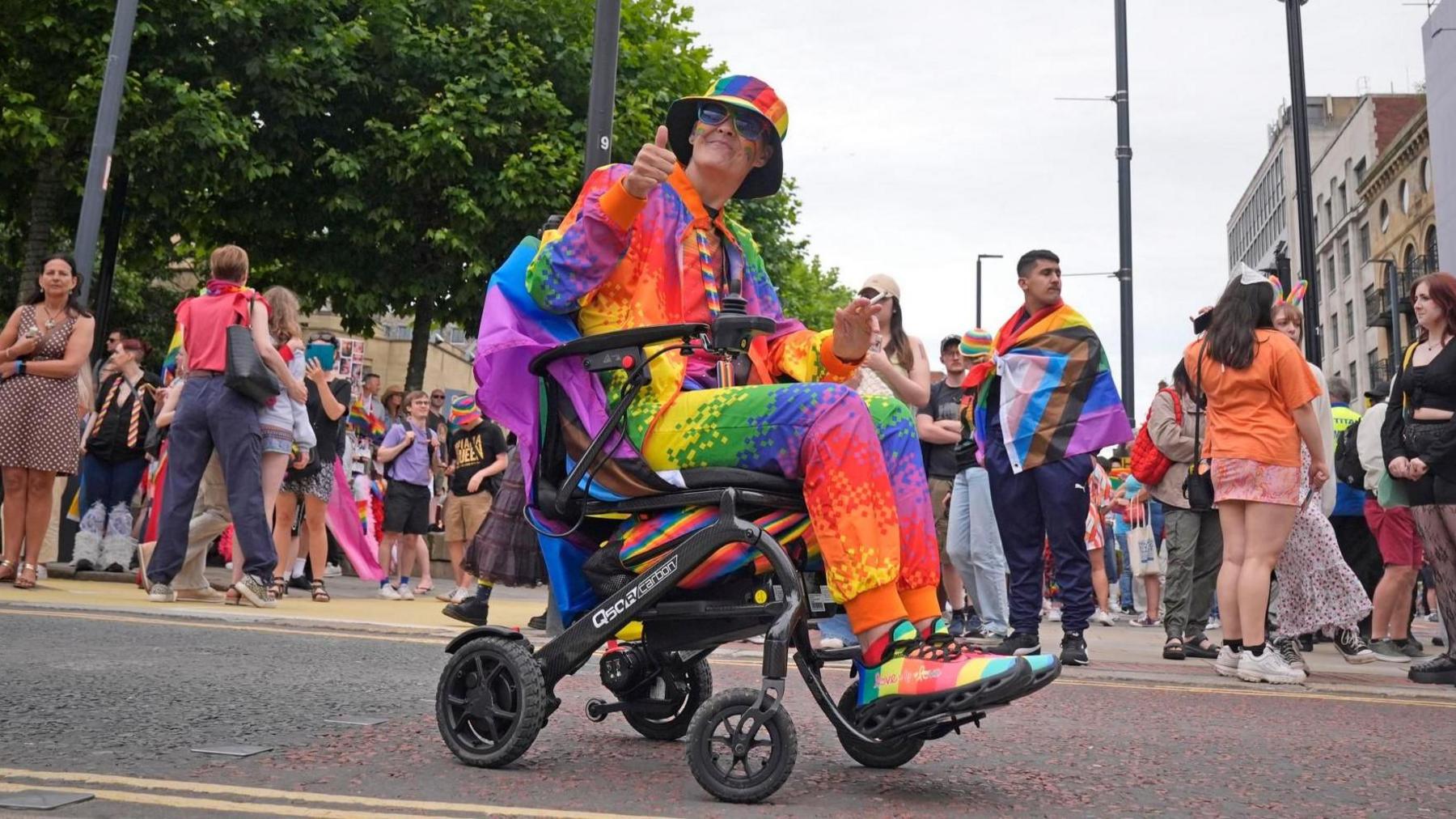 A person in a wheelchair wearing a rainbow suit