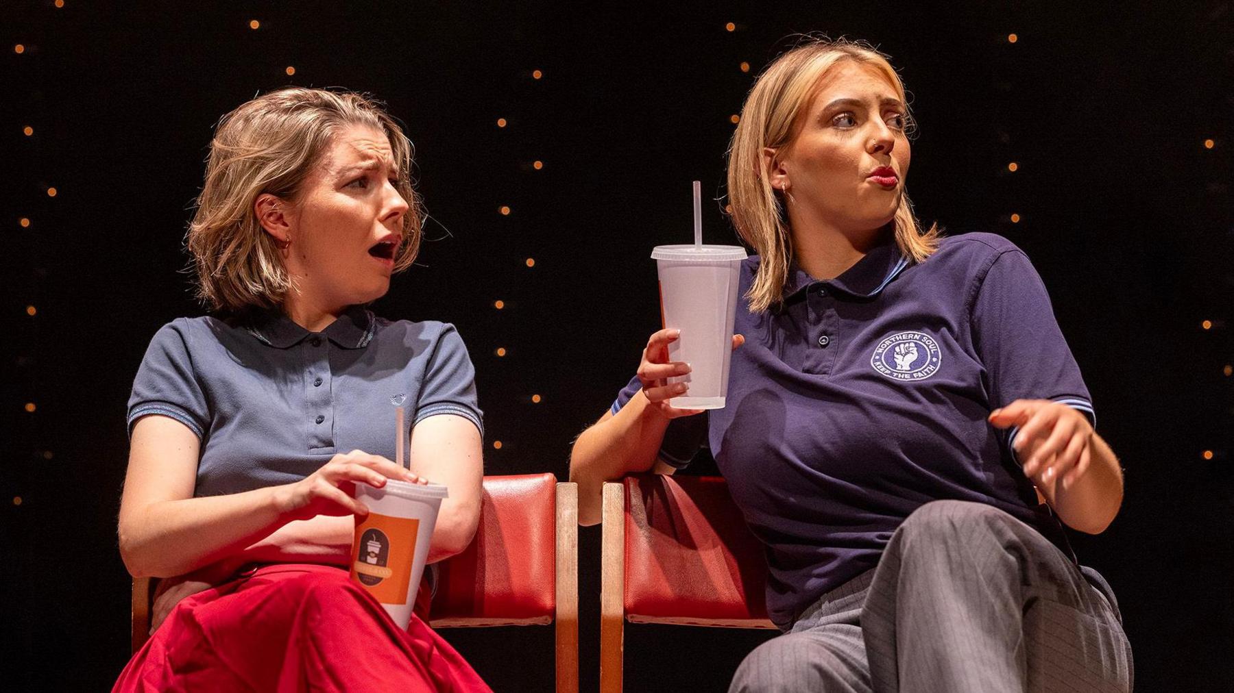 Two actors on stage holding drinks